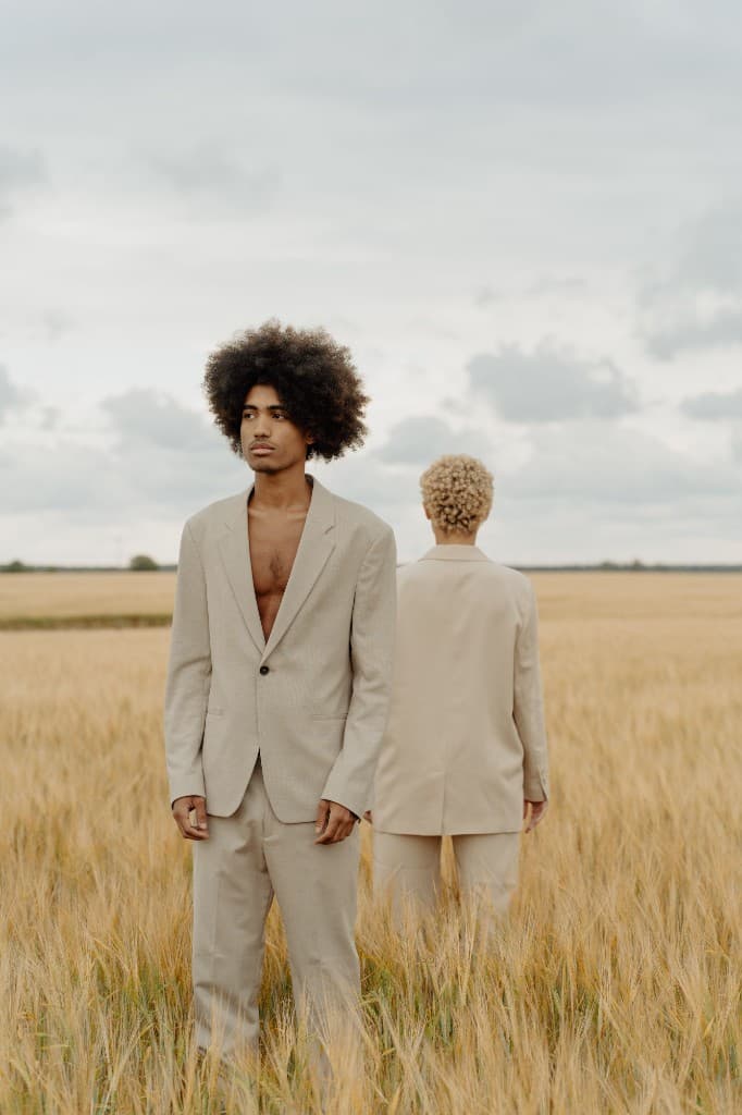Two models in beige suits standing in a wheat field