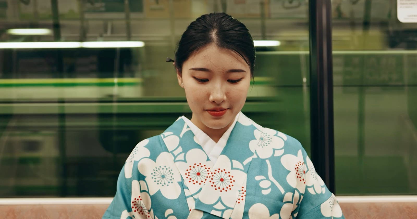 A woman in a teal kimono sitting by a train window