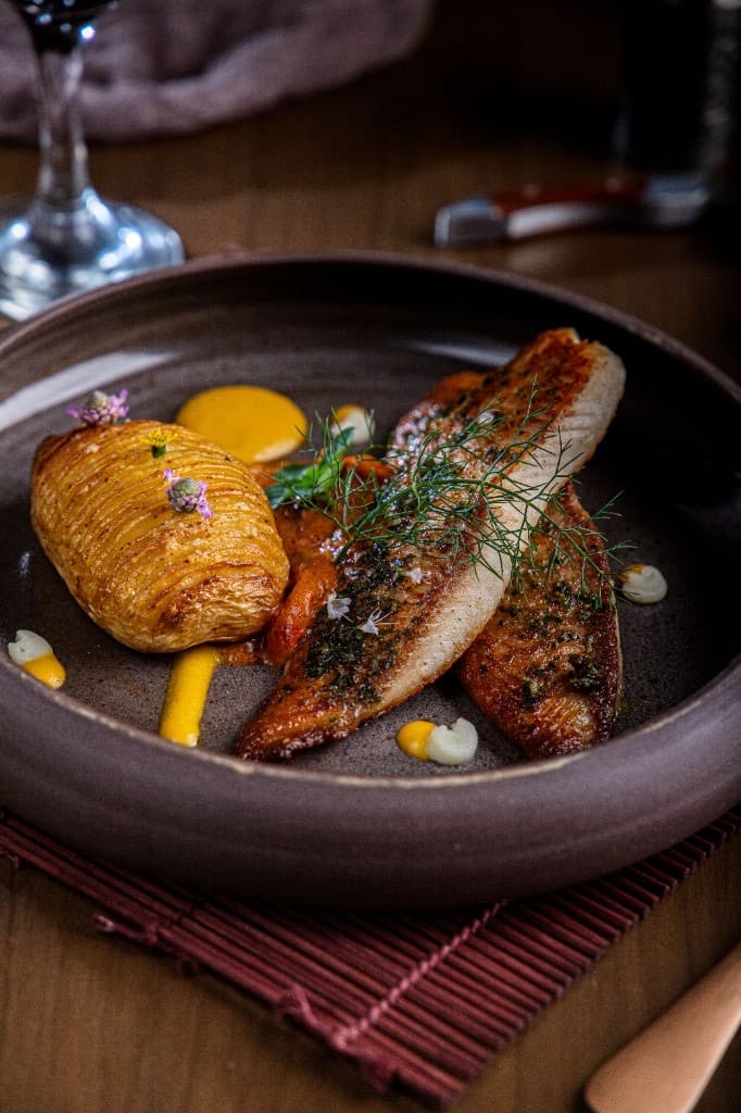 A plated fish dish with roasted potato in a ceramic bowl