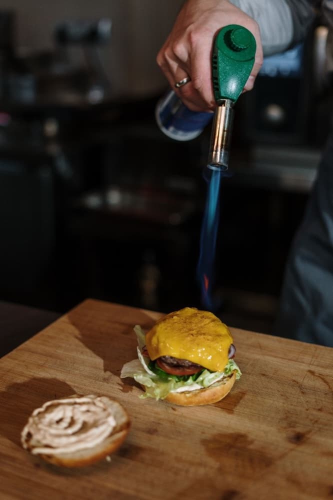 A chef torching cheese on a burger